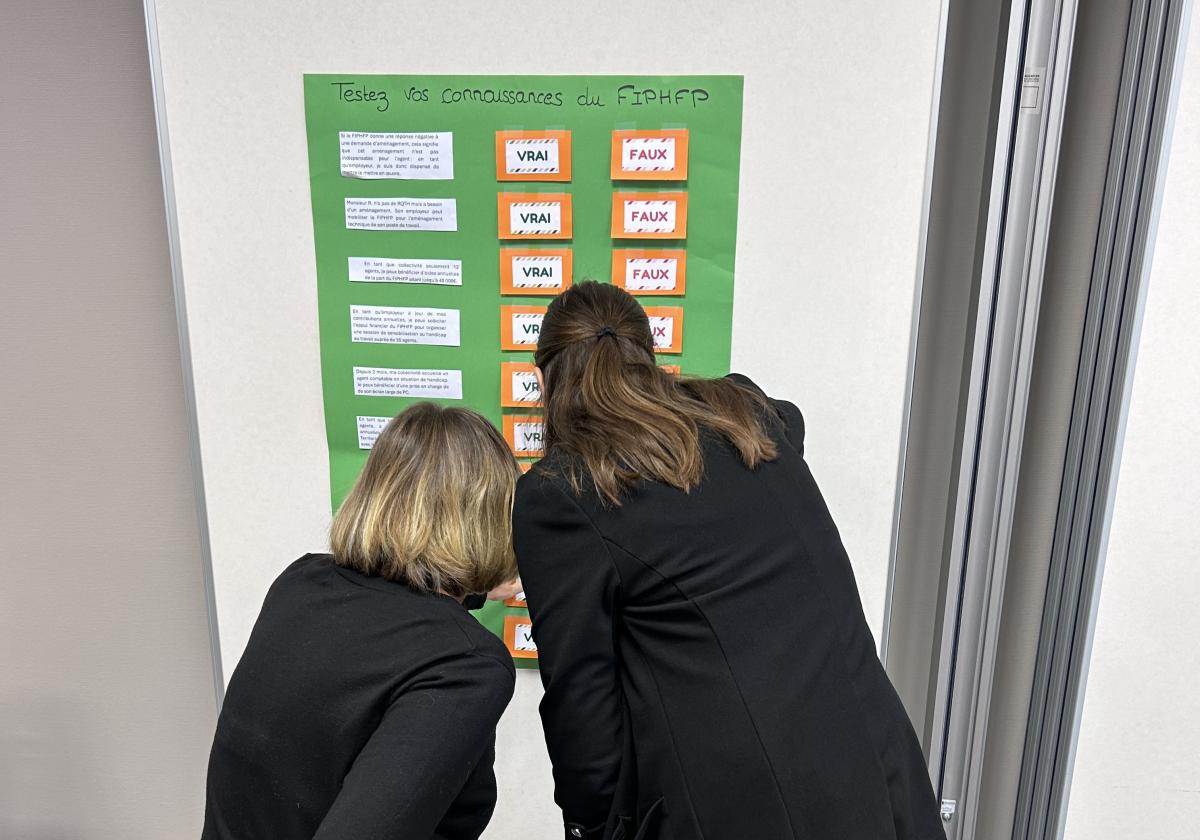 Un questionnaire sur le FIPHFP est accroché au mur et deux personnes tentent d'y répondre.