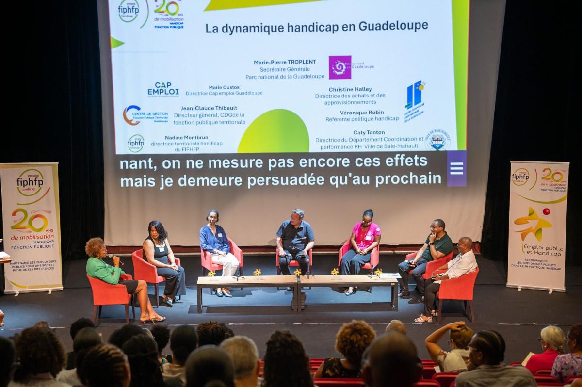 Vue des participants à la table ronde, assis dans des fauteuils devant l'écran